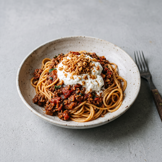 Bord spaghetti met bolognaisesaus, een romige burratacrème en een crumble van krokante ajuintjes
